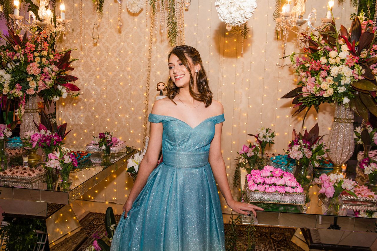 Teenage girl in a glamorous blue gown enjoying her birthday celebration surrounded by colorful floral decorations.
